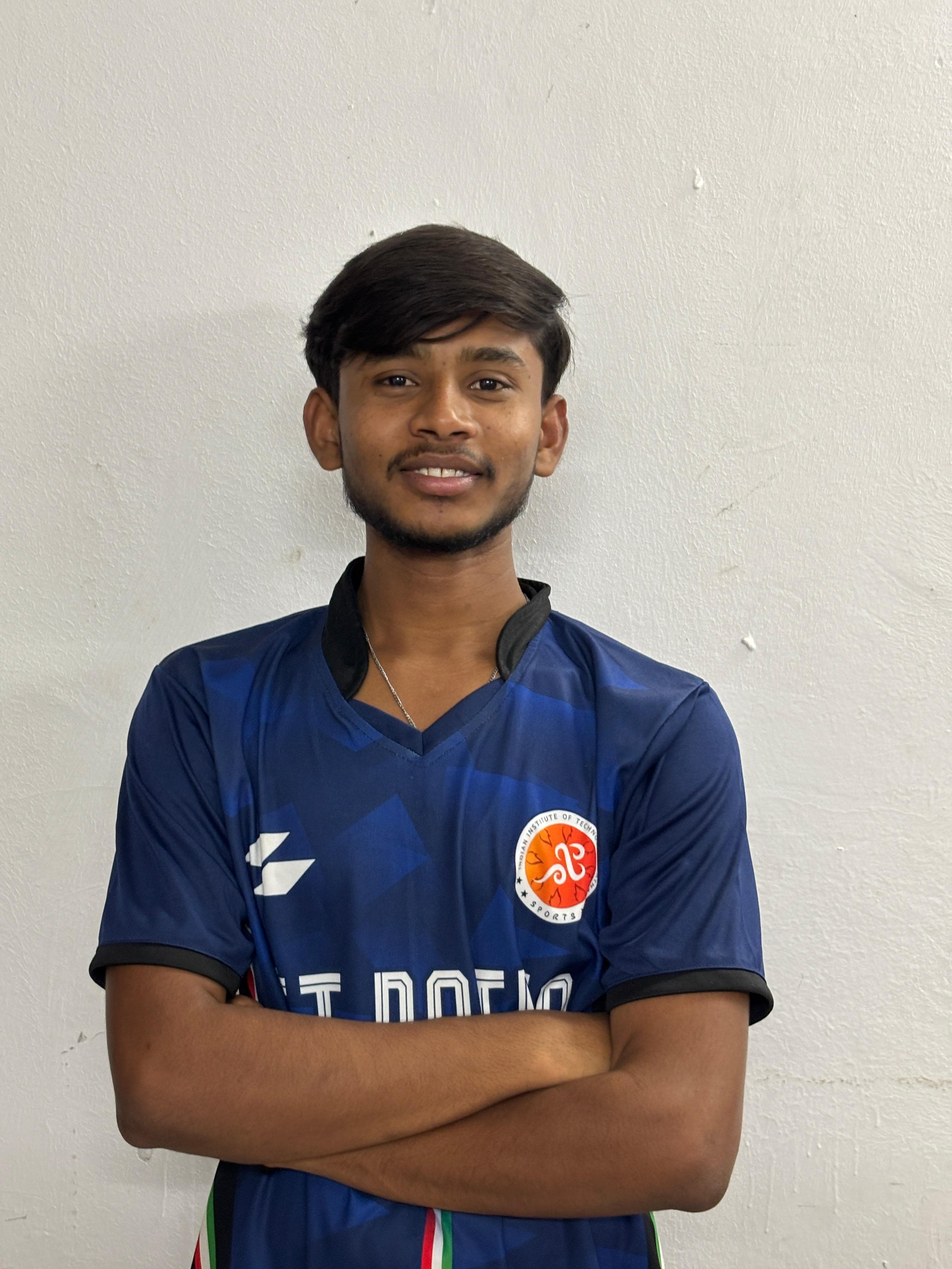 Smiling young man wearing a blue Indian Institute of Technology sports jersey with arms crossed.